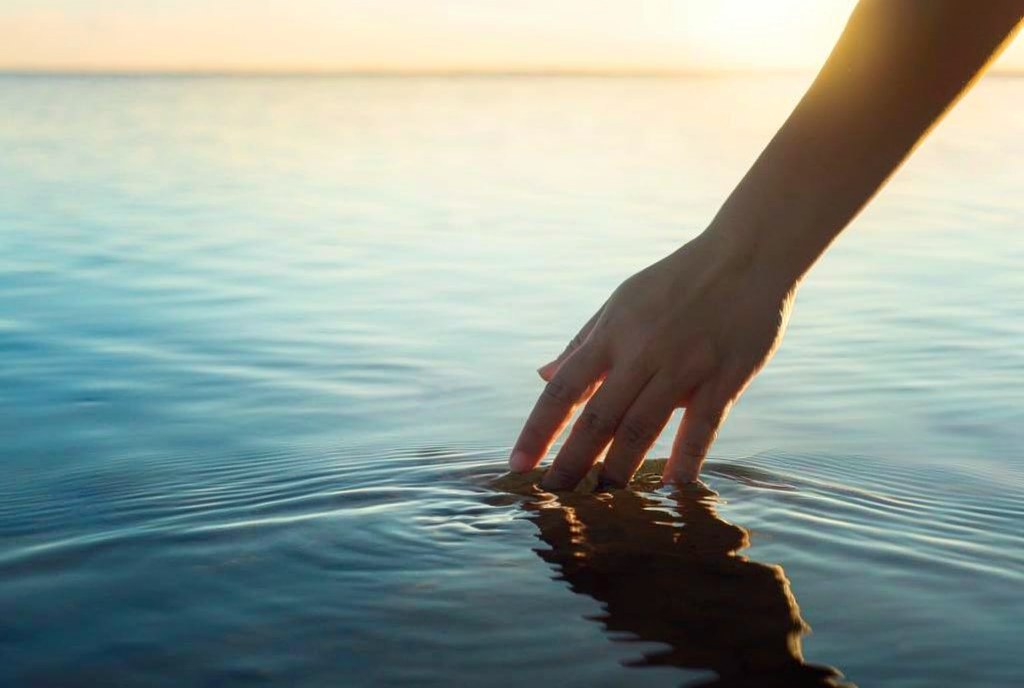A hand gently touching calm water at sunset
